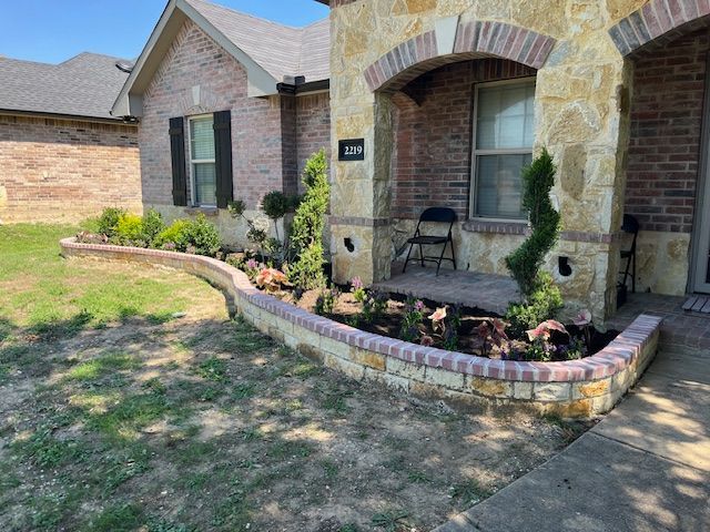 Curved brick-and-stone bed with topiaries and caladiums along a stone porch