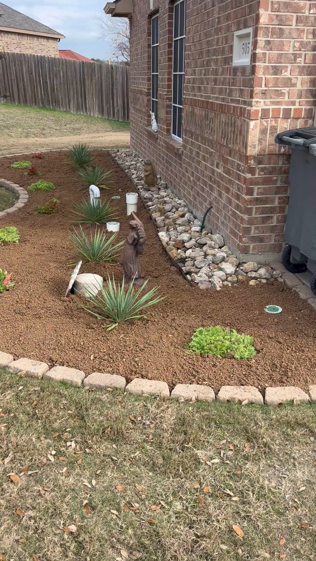 Low-water bed with yuccas, river rock border and stone edging beside a brick home