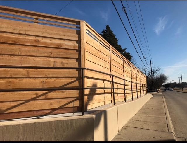 Long horizontal cedar fence with steel railing atop a concrete retaining wall