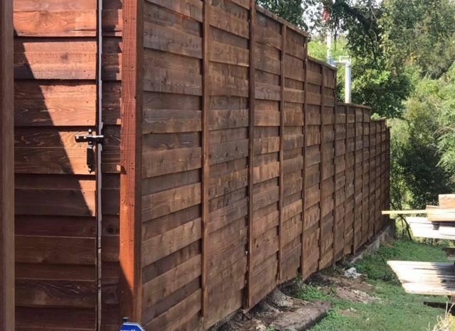 Stained horizontal board fence with a matching gate along a wooded slope