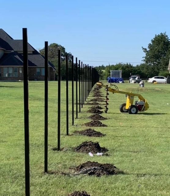 Row of new black steel fence posts set with an auger across a large lawn