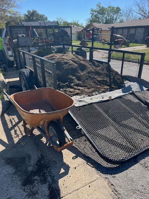 Trailer loaded with fresh soil beside a wheelbarrow, ready for a yard project