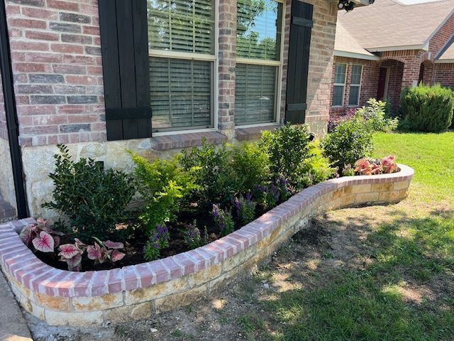 Brick-capped stone raised bed with shrubs, salvia and caladiums under a window