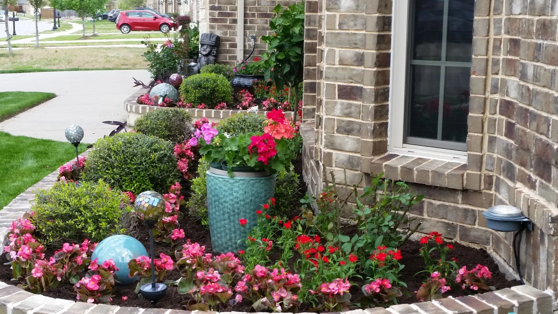Flower bed with a teal accent planter, begonias, boxwoods and garden globes