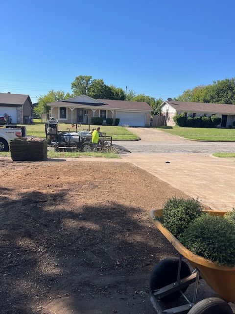 Prepared bare front yard with sod pallet, crew trailer and shrubs ready to plant