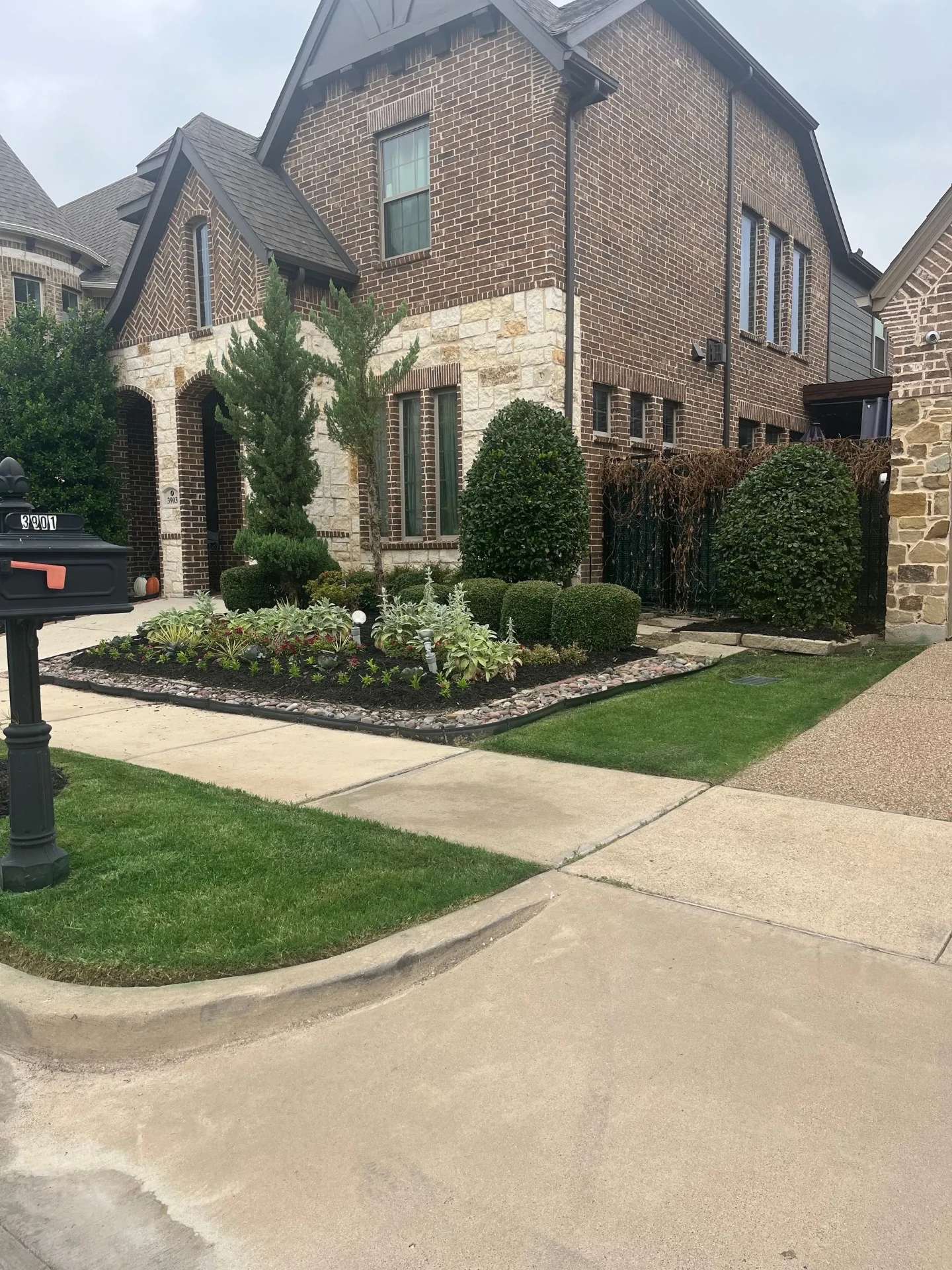 Front bed with river rock border, boxwoods, hostas and evergreens beside a brick home