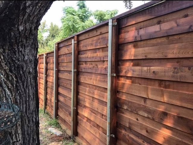 Stained horizontal cedar fence on steel posts beside a large oak tree