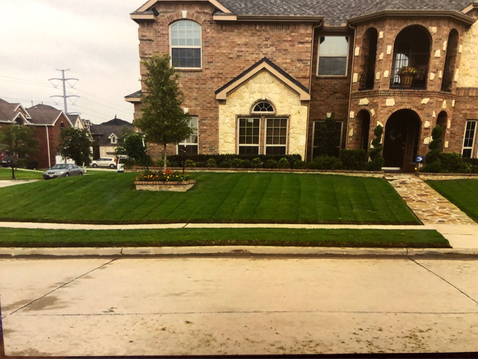 Freshly striped front lawn with a stone planter in front of a large brick home