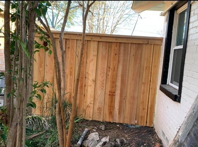 New board-on-board cedar fence closing off a side yard beside a white brick home