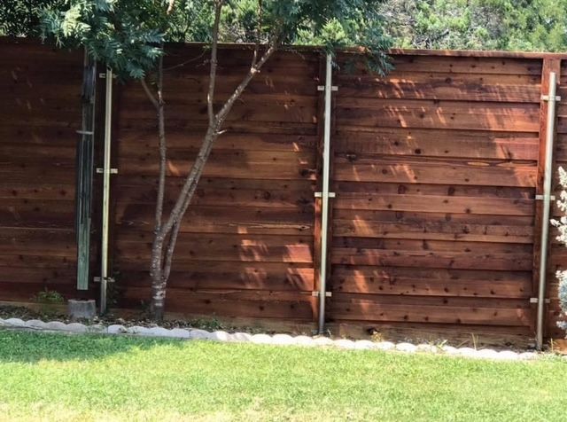 Stained horizontal cedar fence on steel posts behind a white stone lawn border