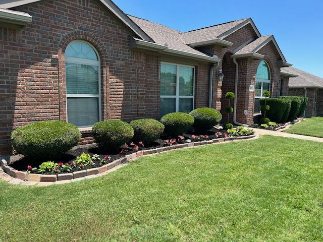 Curved paver-edged bed with rounded shrubs and red flowers along a brick home